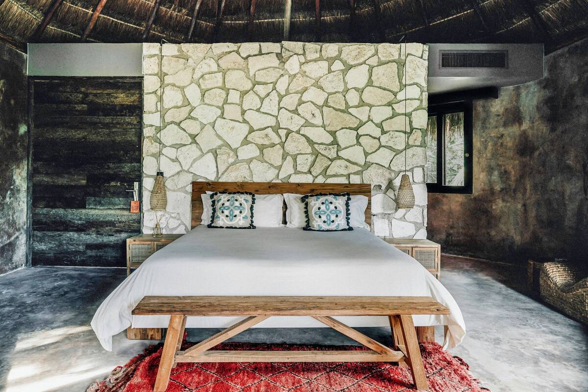 Un dormitorio con pared de piedra, estructura de cama de madera y alfombra roja.