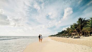 A beach with a couple walking along the shore, palm trees, and beach huts.