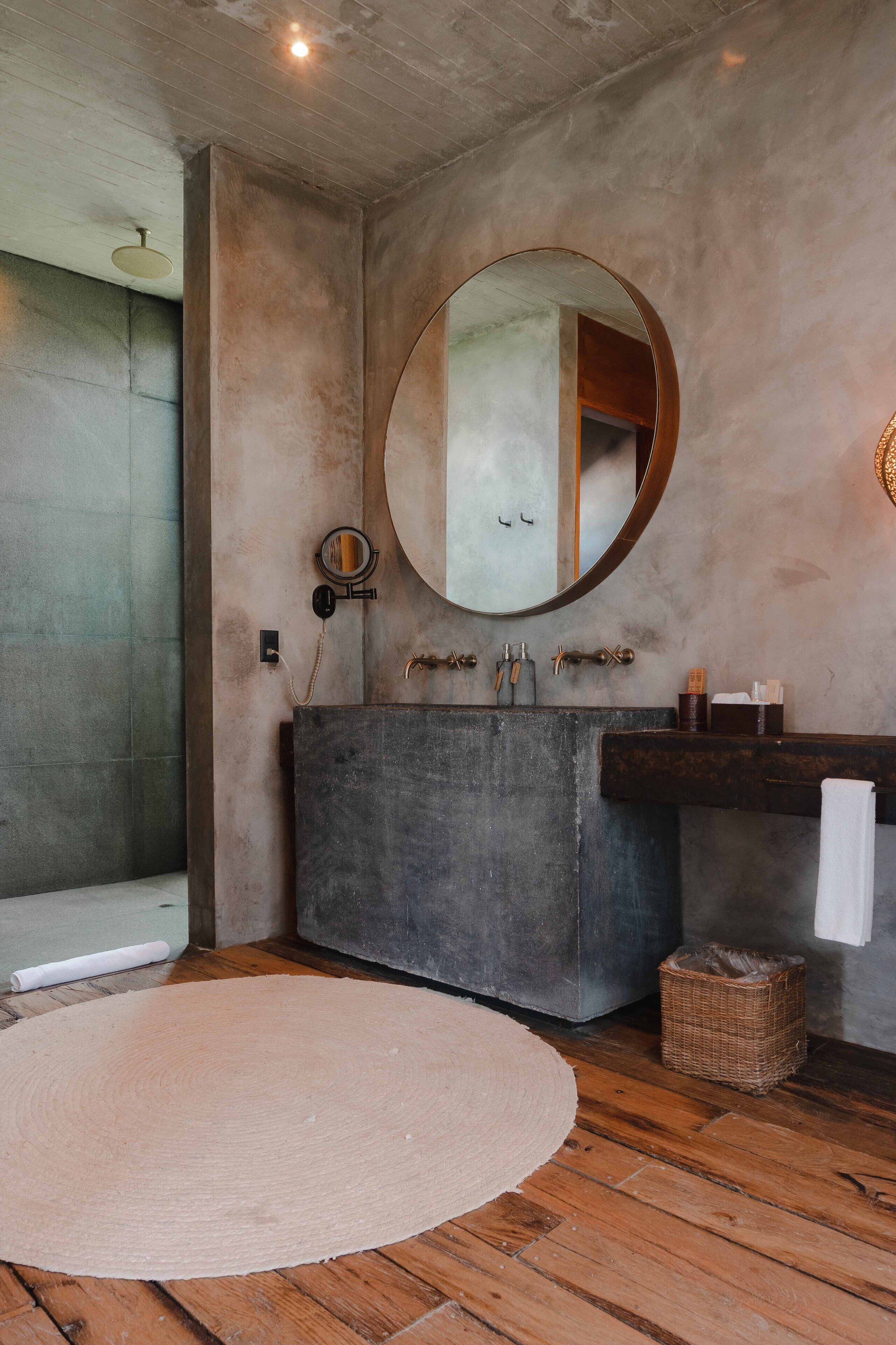 Une salle de bain avec un miroir rond, un meuble-lavabo en bois et un tapis rond sur le sol.