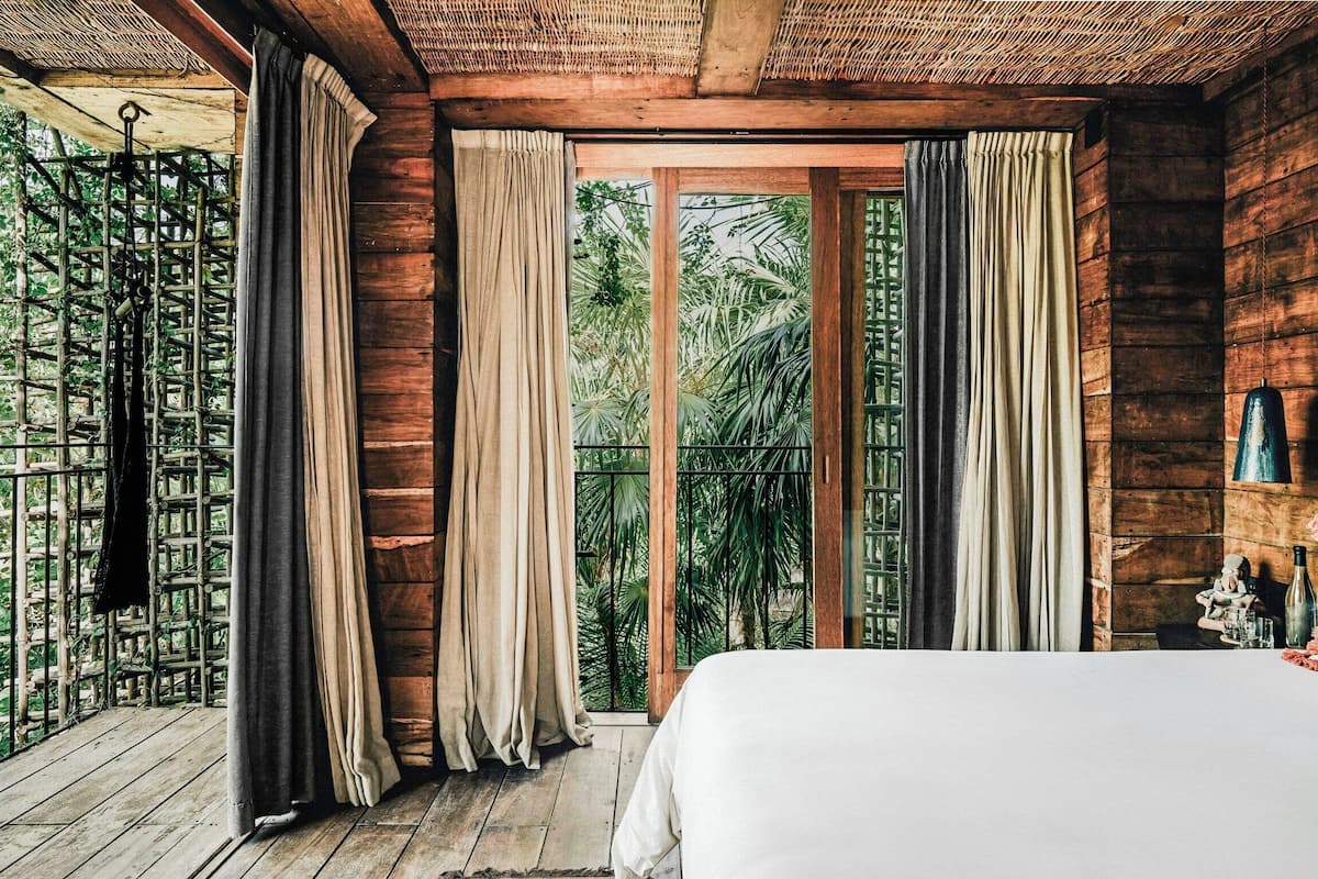Un dormitorio con una cama grande, paredes de madera, un balcón con cortinas y vistas a zonas verdes.
