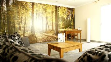 Un salón con un mural de un bosque, una mesa de centro de madera y un sofá con cojines estampados.