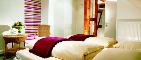 A hotel room with a bed, a wicker chair, a small table with a vase of flowers, and a striped wall.