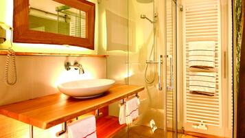 Un baño con tocador de madera, cabina de ducha con vidrio y perchero con varias toallas.