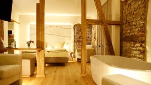 A modern bedroom with a large bed, a sitting area with a sofa, and a separate bathroom with a bathtub. - Flair Hotel Nieder (Bestwig)