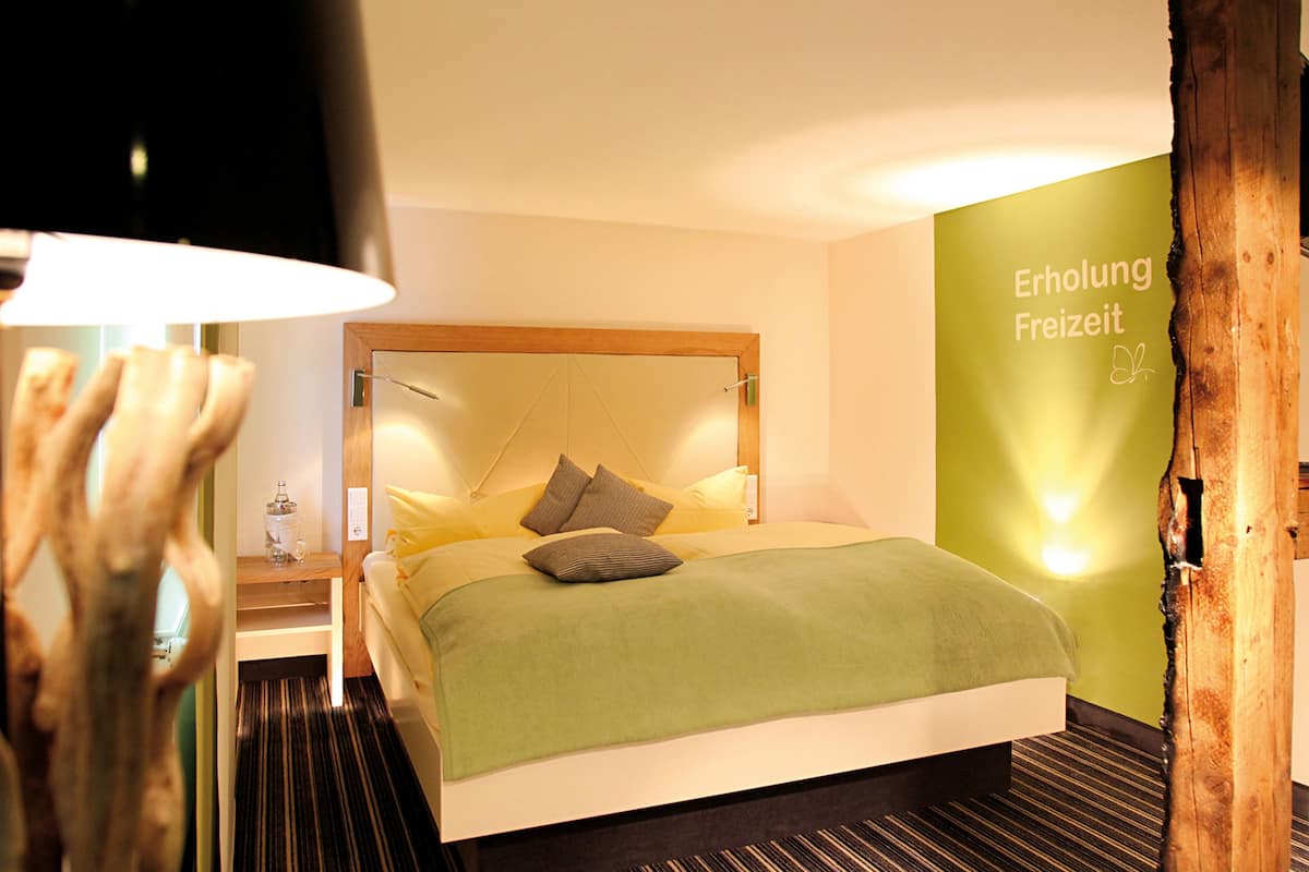 Moderni hotellihuone, jossa on suuri sänky, yöpöytä, lamppu ja vihreä seinä, jossa on tekstiä.