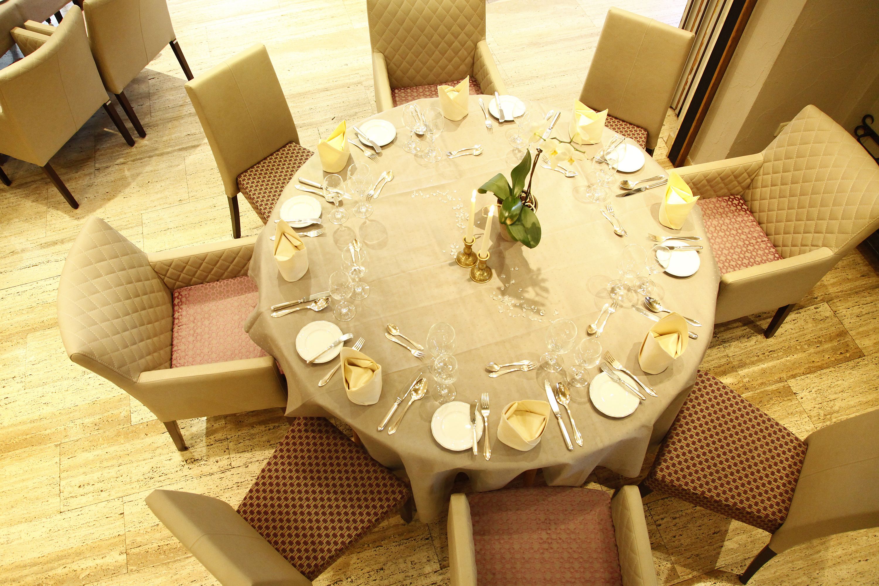 Mesa redonda para seis personas, con mantel blanco, detalles dorados y un arreglo floral en el centro.