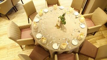 Mesa redonda para seis personas, con mantel blanco, detalles dorados y un arreglo floral en el centro.