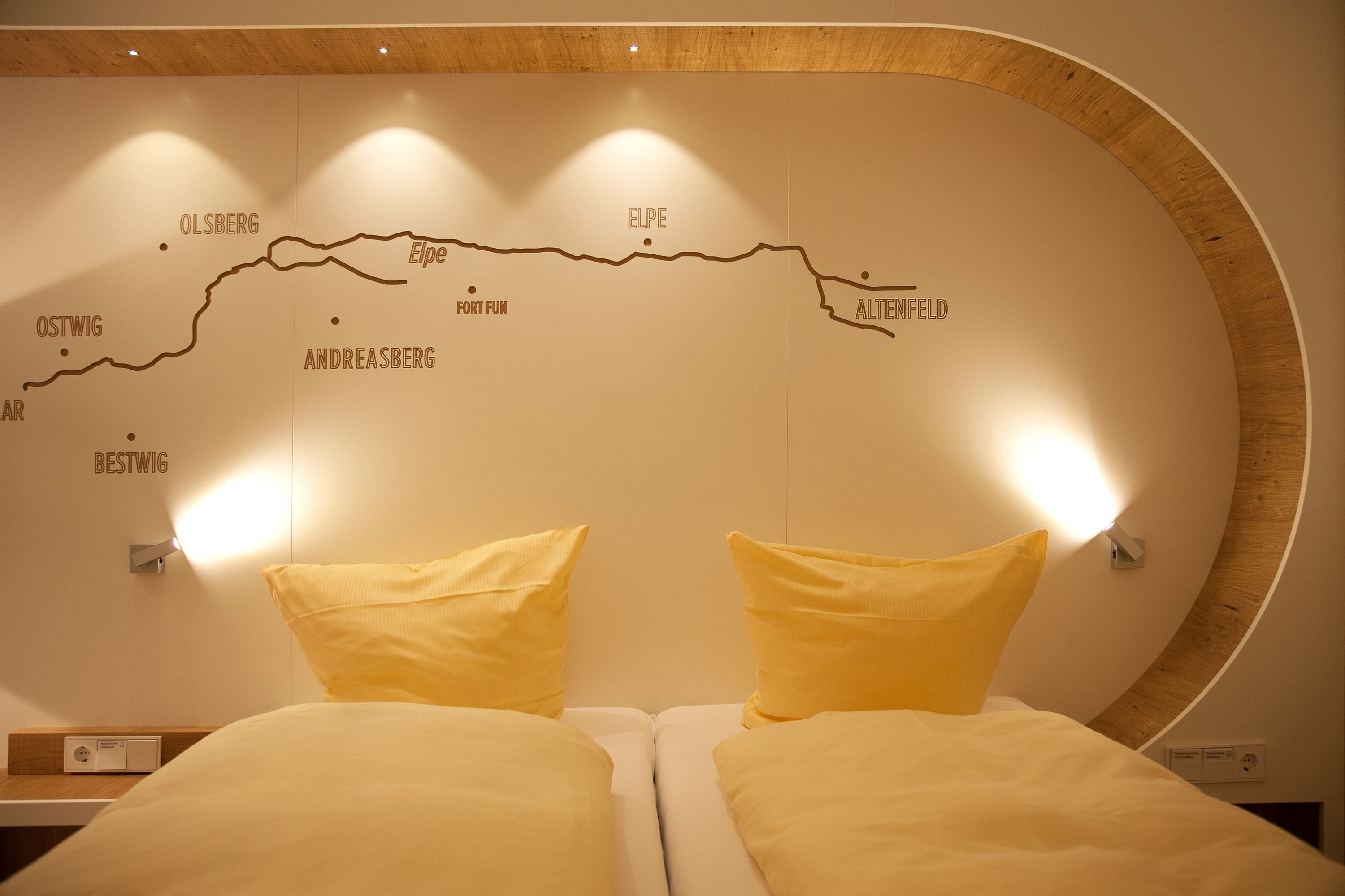 Ein Hotelzimmer mit einem Bett, zwei Kissen, einem Nachttisch und einer Wandkarte, die nahegelegene Orte hervorhebt.