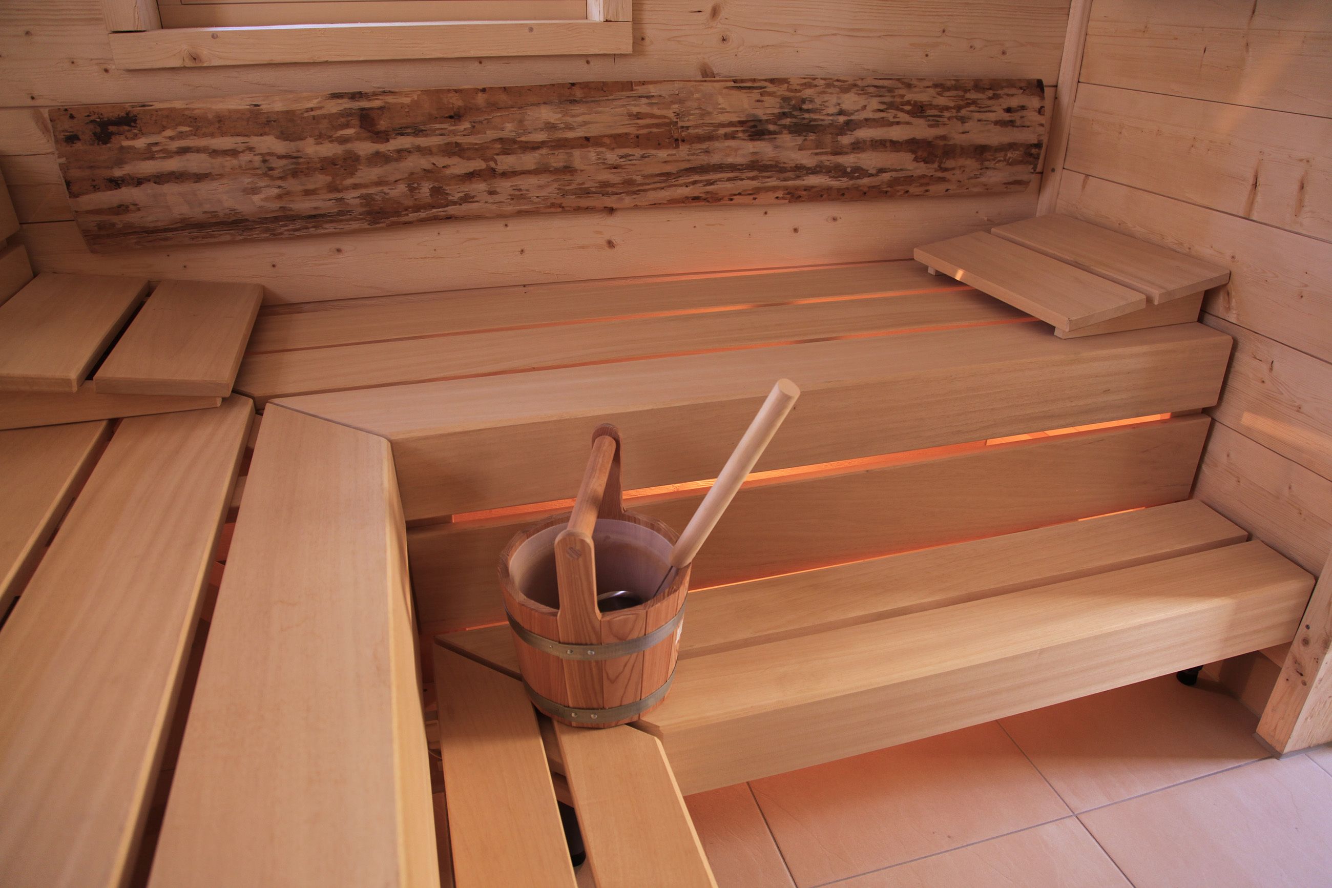 Una sauna con bancos de madera y un balde de madera con una cuchara.