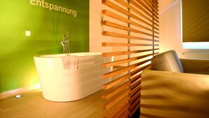 A modern bathroom with a freestanding bathtub, a wooden slatted partition, and a green accent wall. - Flair Hotel Nieder (Bestwig)