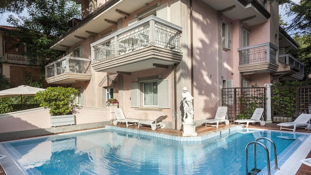A swimming pool with lounge chairs and a statue, surrounded by a building with balconies. - Residence Villa Lidia (Riccione)