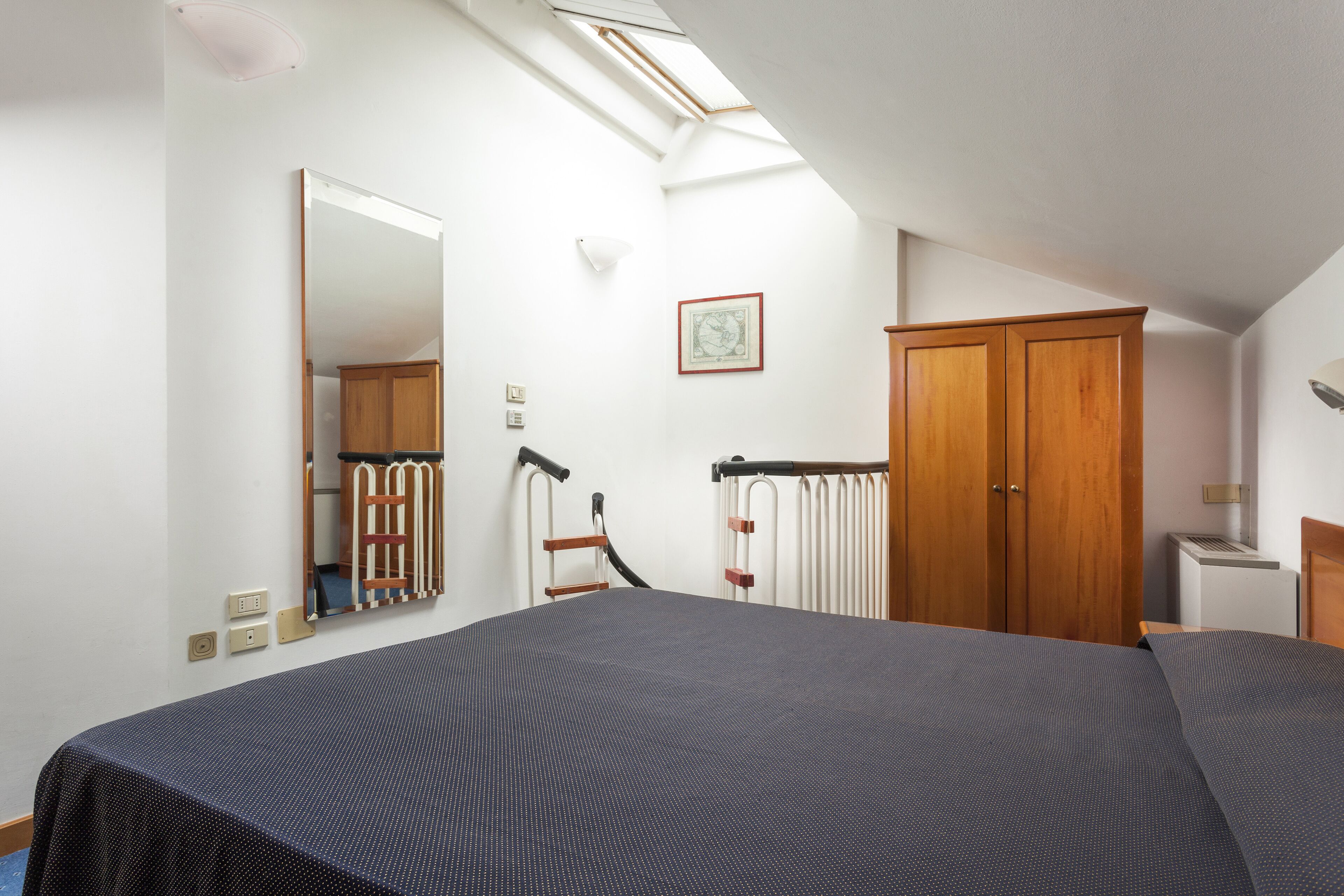 Une chambre avec un grand lit, une lucarne, une armoire et un radiateur.