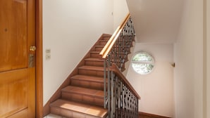 A staircase with wooden steps and metal railings, a wooden door with a brass handle, and a small window with a view of greenery. - Residence Villa Lidia (Riccione)