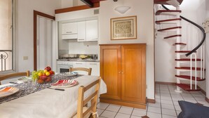 A dining area with a table set for two, a wooden cabinet, and a spiral staircase. - Residence Villa Lidia (Riccione)