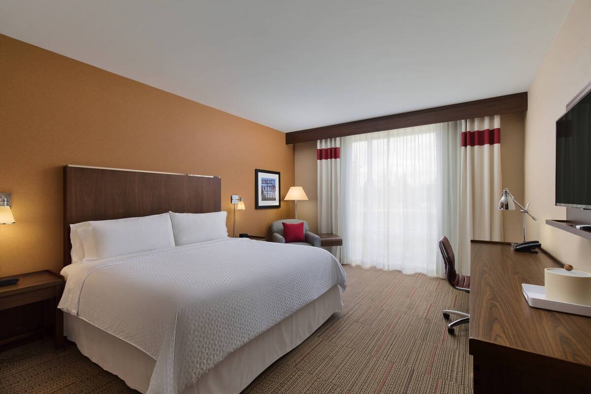 Une chambre d’hôtel avec un grand lit, un bureau, une chaise, une télévision et une fenêtre avec des rideaux.