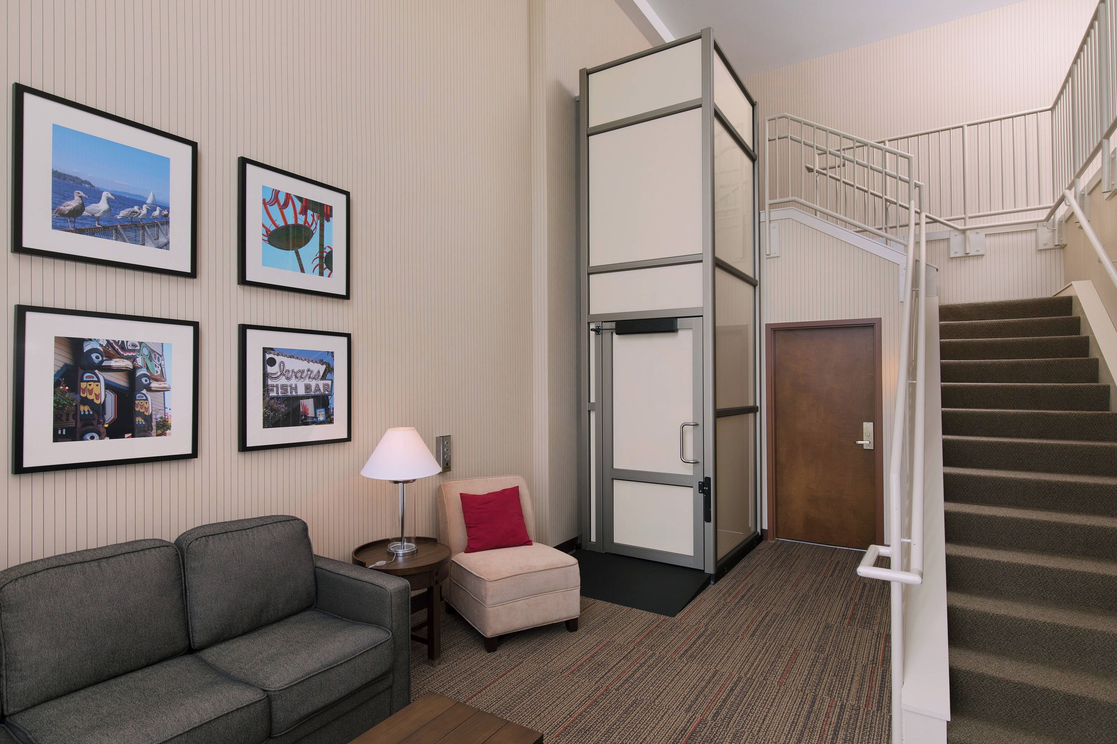 A hotel room with a sofa, a small table with a lamp, a door, and a staircase.