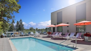A pool area with lounge chairs and umbrellas, surrounded by a modern building.