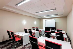 A conference room with tables and chairs, a projector screen, and a carpeted floor. - Four Points By Sheraton Seattle Airport South (Des Moines)