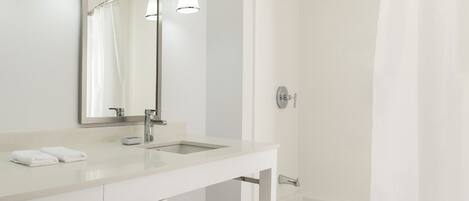 Un baño moderno con tocador blanco, un espejo grande, dos lavamanos, una ducha con puerta de cristal y un perchero para toallas.