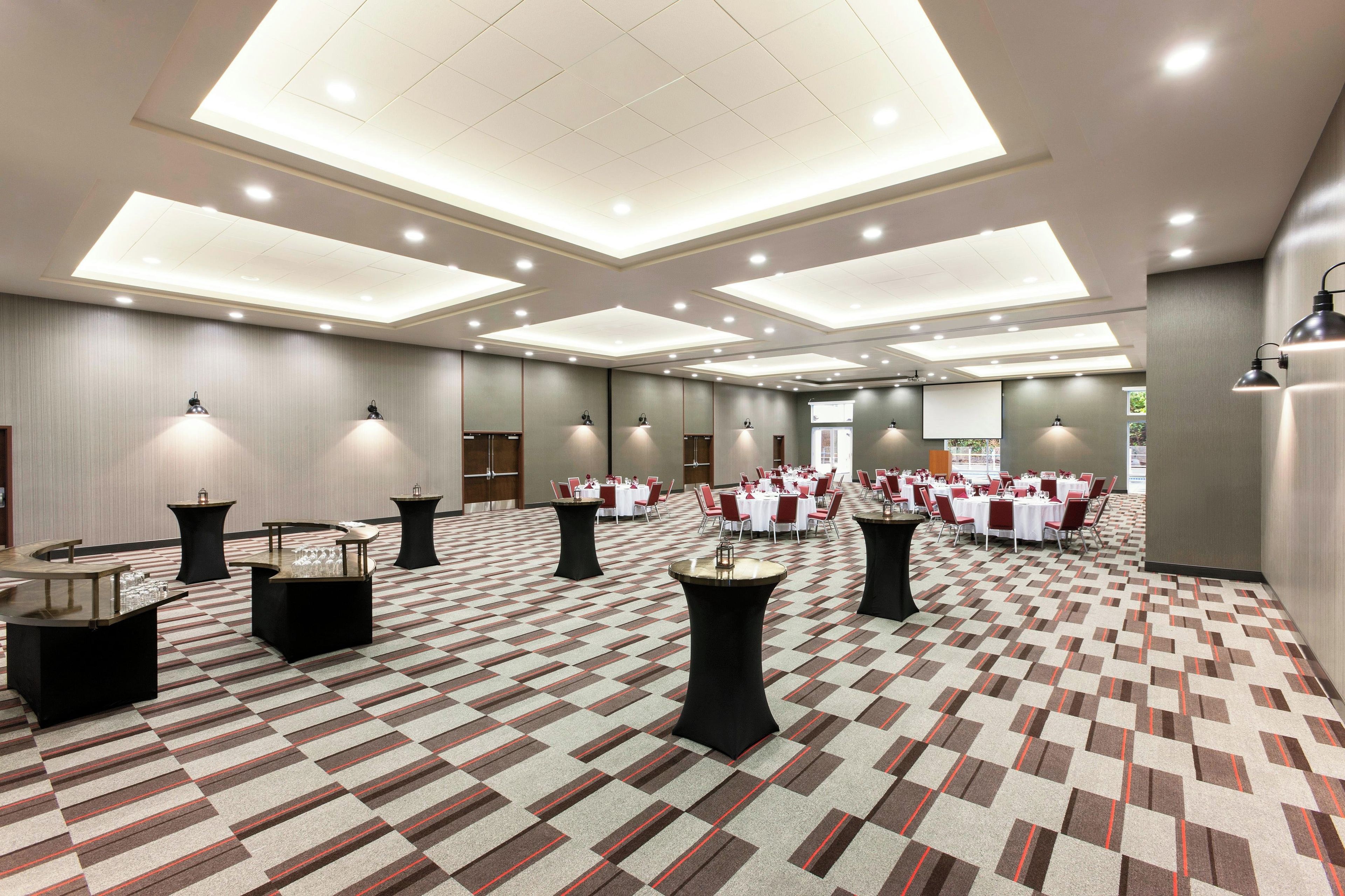 Een hotelconferentiezaal met meerdere tafels en stoelen, een kamerbreed tapijt en inbouwverlichting.