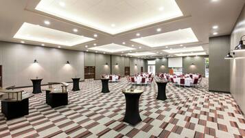 Een hotelconferentiezaal met meerdere tafels en stoelen, een kamerbreed tapijt en inbouwverlichting.