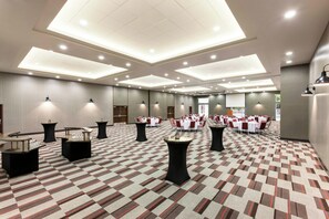 Een hotelconferentiezaal met meerdere tafels en stoelen, een kamerbreed tapijt en inbouwverlichting.