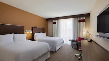 A hotel room with two beds, a desk, a chair, a TV, and a window with curtains.