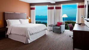 A hotel room with a large bed, a desk, a chair, and a view of mountains through the window.