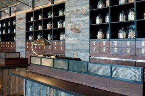 Een opslagruimte met metalen schappen vol potten en dozen, een metalen bureau met een lamp, en een houten wand met een rasterpatroon.