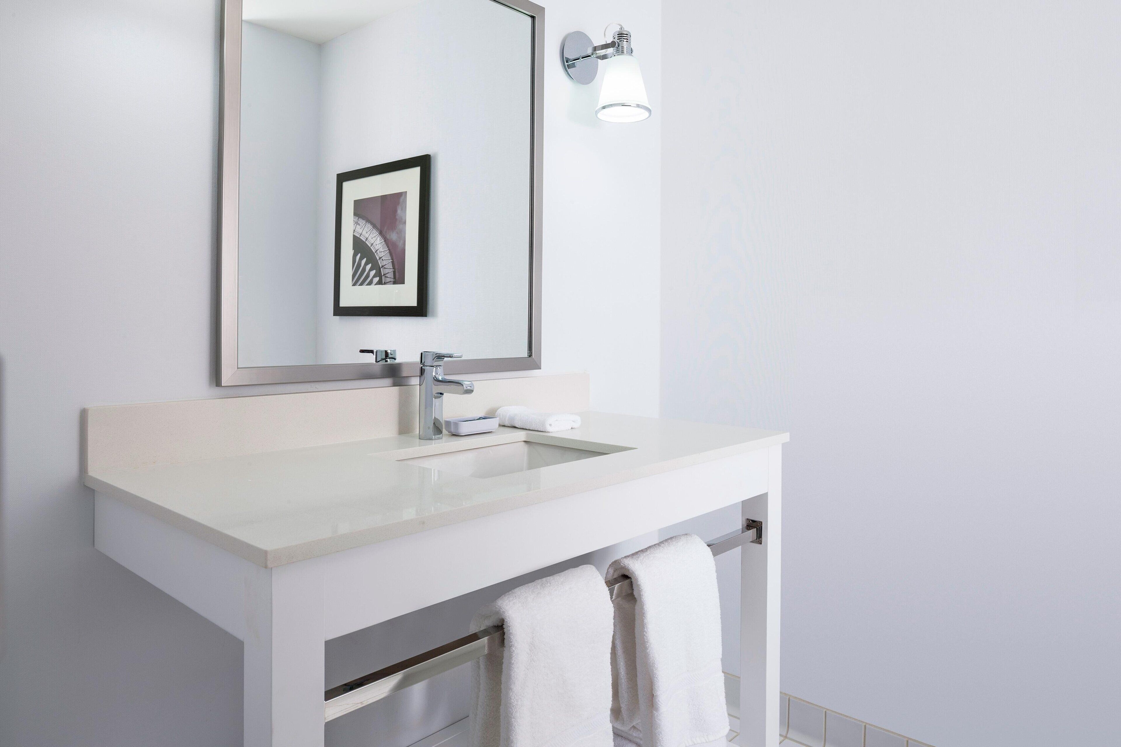 A modern bathroom with a white sink, a large mirror, and a framed picture above the mirror.