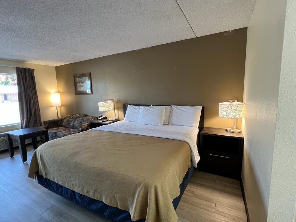 A hotel room with a large bed, two bedside tables with lamps, a chair, and a window with curtains.