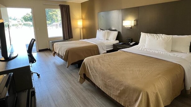 Une chambre d’hôtel avec deux lits, un bureau avec une chaise, une télévision et une fenêtre avec des rideaux.