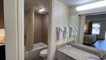 Un bagno con vasca, water e lavandino, asciugamani appesi al muro e uno specchio sopra il lavandino.