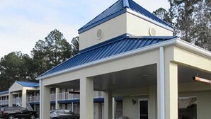 Un motel doté d’un parking couvert, de nombreuses chambres et d’un bâtiment principal surmonté d’un toit bleu.