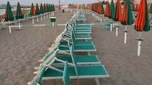 A beach with rows of green lounge chairs and orange umbrellas. - Residenza Kenzia (Cattolica)