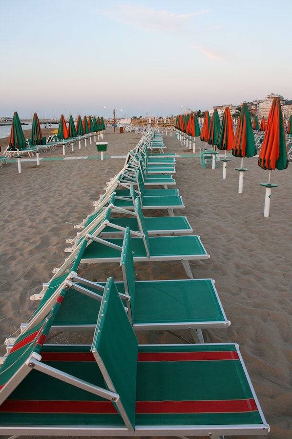 A beach with rows of green lounge chairs and orange umbrellas.