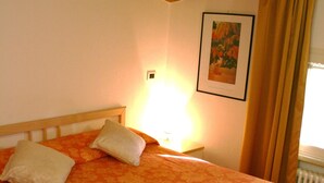 A bed with an orange floral bedspread, two pillows, and a folded towel on a wooden bed frame in a room with a wooden ceiling and a framed picture on the wall. - Residenza Kenzia (Cattolica)