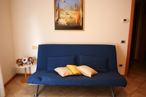 A blue sofa with two pillows, a small table with a teddy bear and a soccer ball, and a framed picture on the wall.