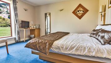Habitación de hotel con una cama grande, un escritorio, una silla, un televisor y una ventana con vistas a la vegetación.
