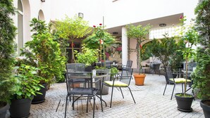 An outdoor patio area with potted plants, outdoor seating, and a view of a building with arches. - Europejski Boutique Hotel (Radom)
