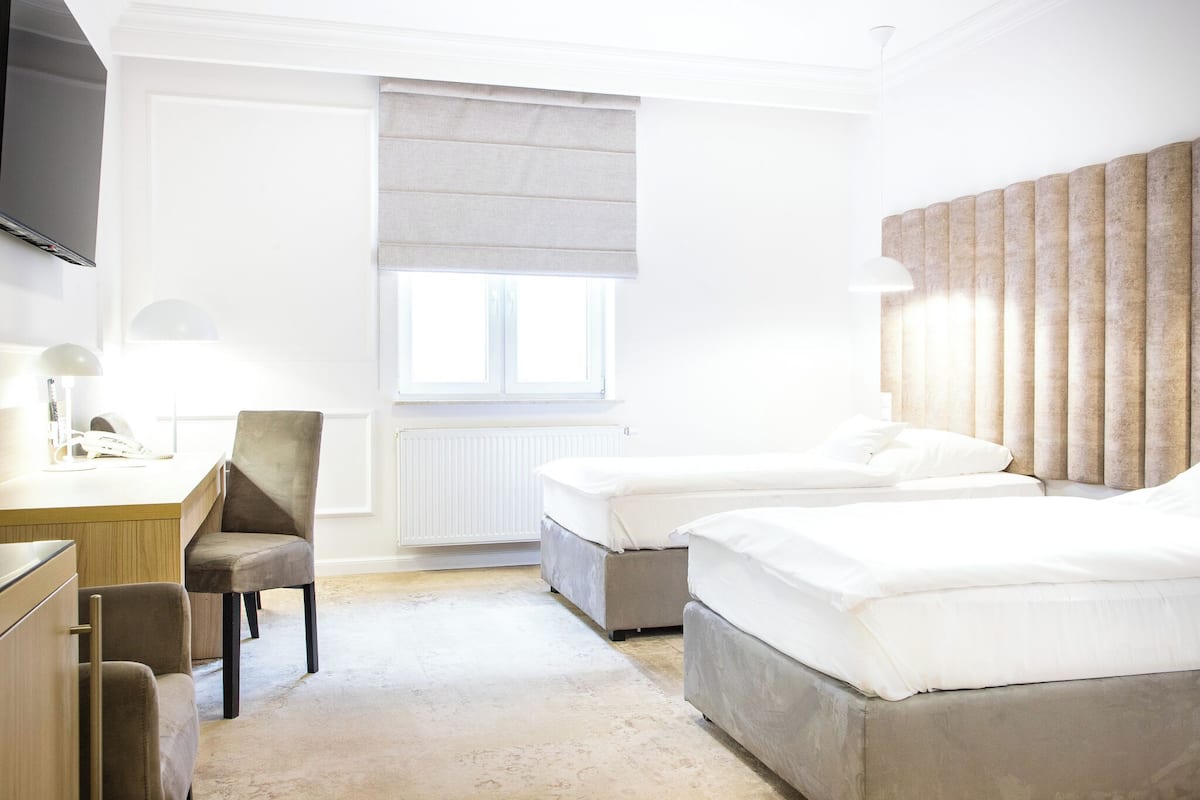 A hotel room with two beds, a desk with a chair, a television, and a window with a blind.