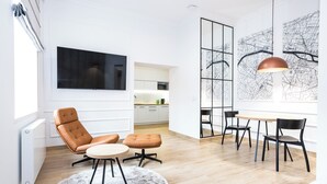 A modern living room with a flat-screen TV, a dining area with a round table and chairs, and a large window with a cityscape view. - Europejski Boutique Hotel (Radom)