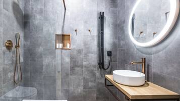 Un baño moderno con una bañera independiente, un espejo redondo, un tocador de madera y una zona de ducha con ducha de mano.
