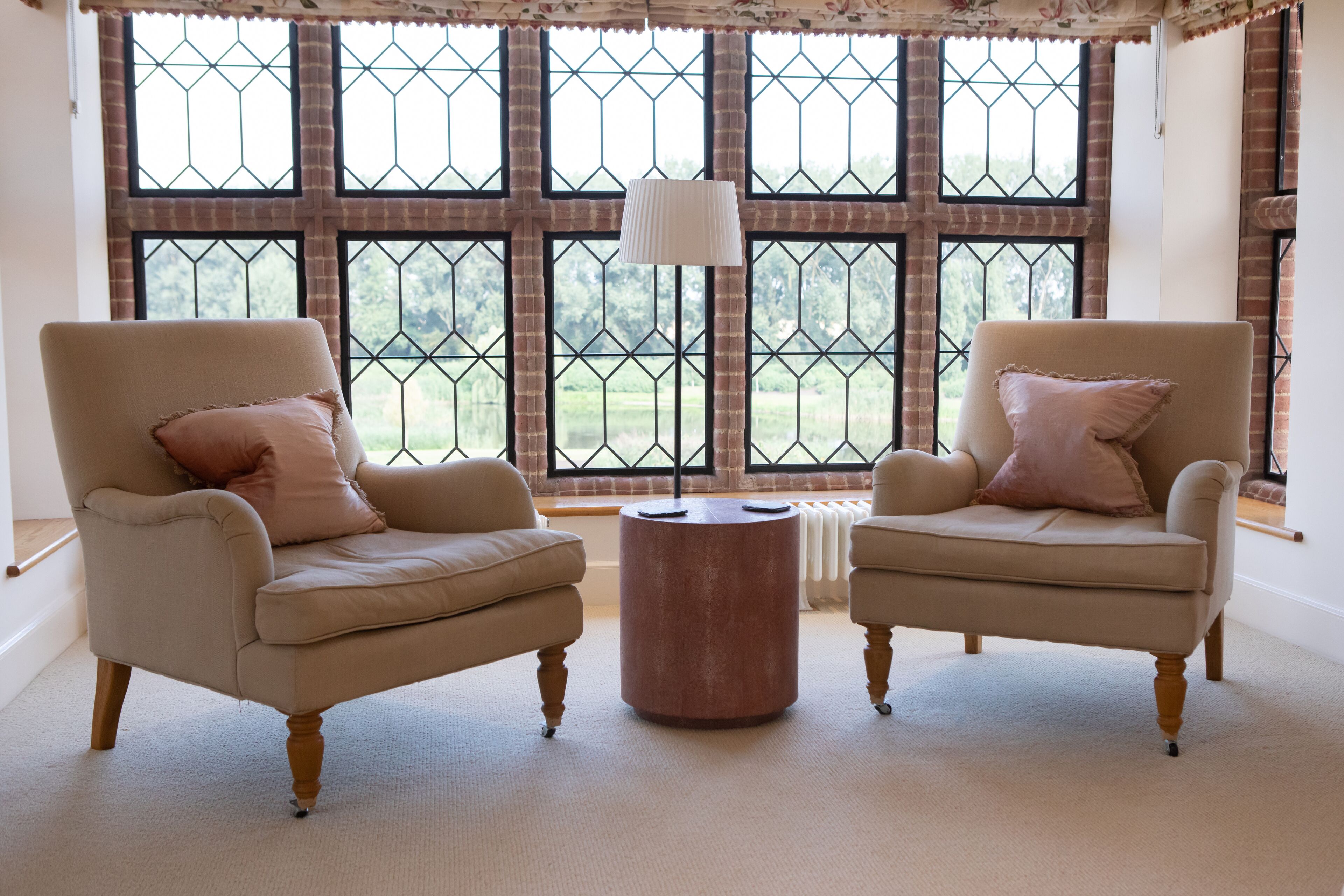 A room with two armchairs, a round wooden table, and a large window with a view of greenery.