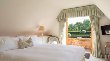 A bedroom with a large bed, a bedside table with a lamp, a mirror, and a view of the garden through open curtains.