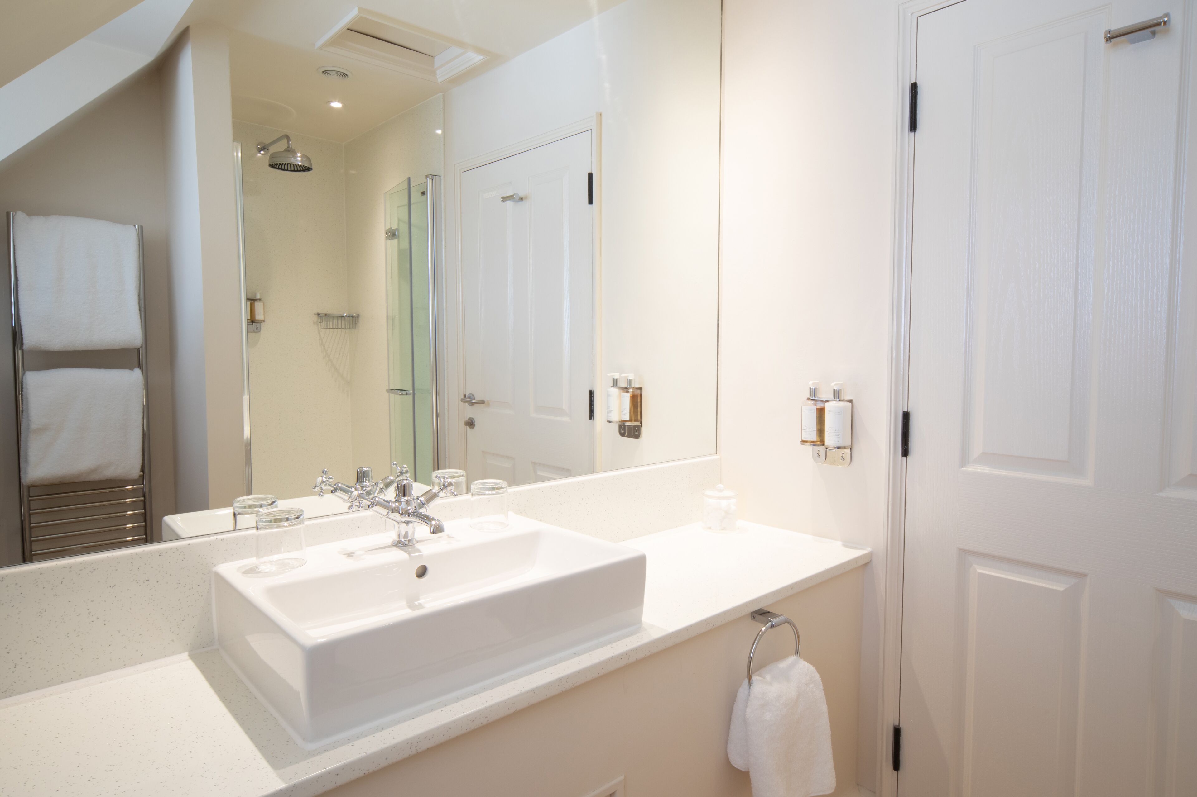 A modern bathroom with a large mirror, two sinks, a shower, and a toilet.