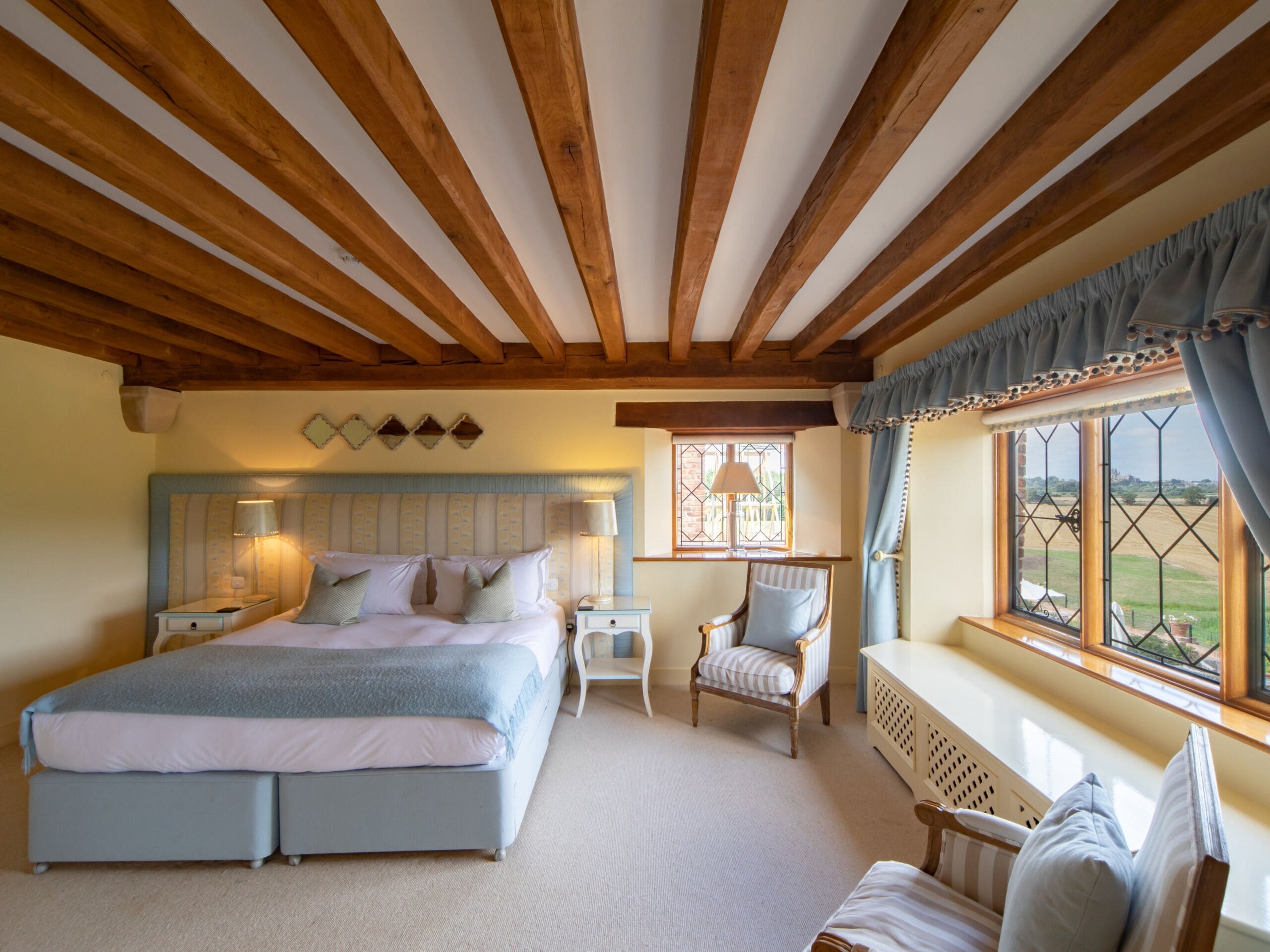 A bedroom with a large bed, a chair, a small table, and a window with a view.
