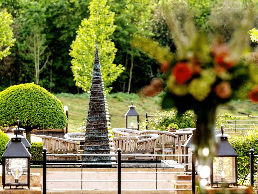 A garden with a central fountain, surrounded by benches and lanterns.