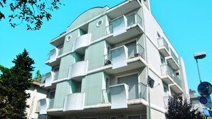 A multi-story building with balconies, a visible street sign, and a clear blue sky. - Residenza Manuela (Riccione)