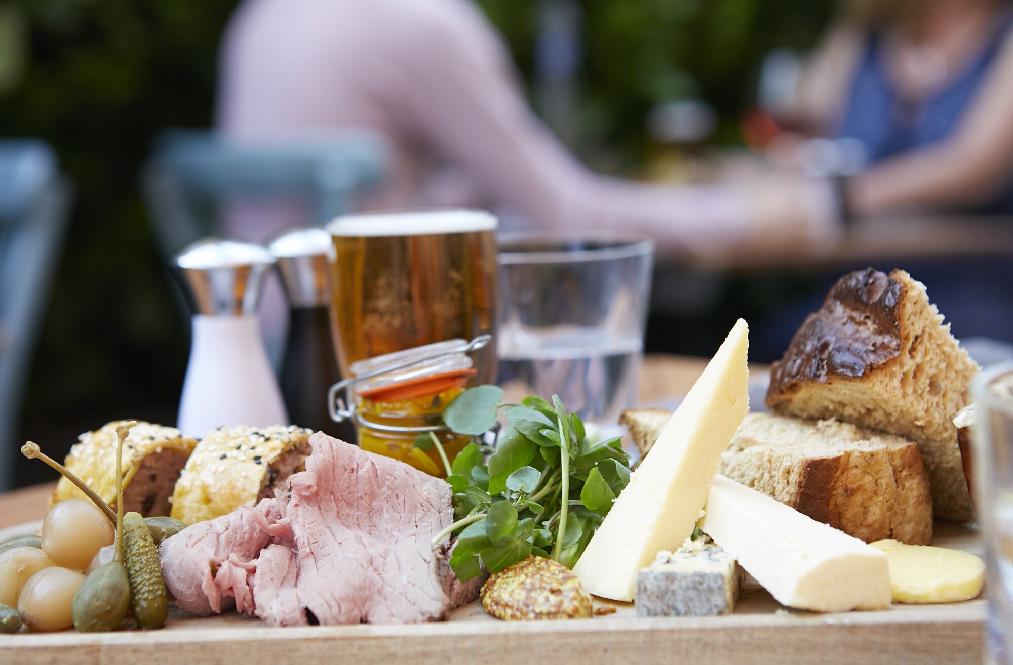 A charcuterie board with various meats, cheeses, and bread, accompanied by pickles and a glass of water.